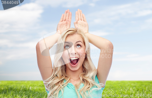 Image of happy smiling young woman making bunny ears