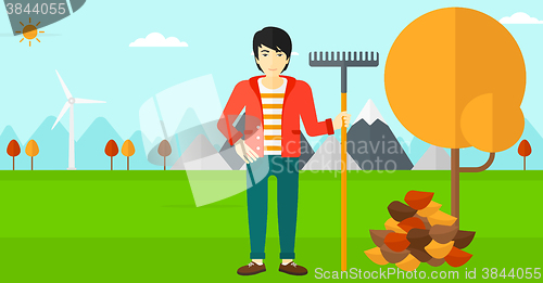 Image of Man with rake standing near tree and heap of autumn leaves.