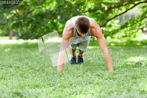 Image of young man doing push ups on grass in summer park