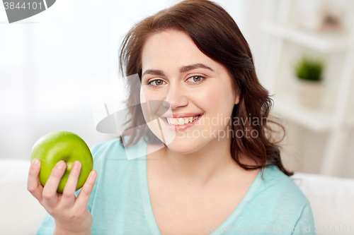 Image of happy plus size woman eating green apple at home