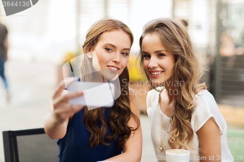 Image of happy women with smartphone taking selfie at cafe