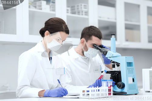 Image of scientists with clipboard and microscope in lab