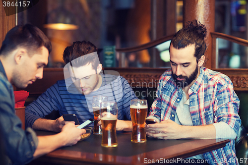 Image of male friends with smartphones drinking beer at bar