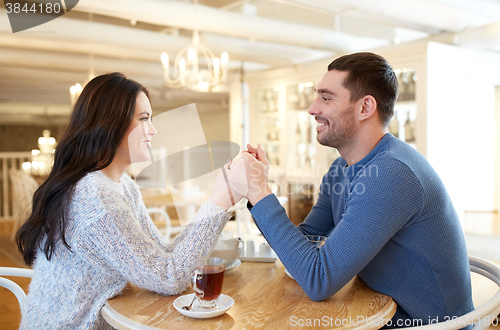 Image of happy couple with tea holding hands at restaurant