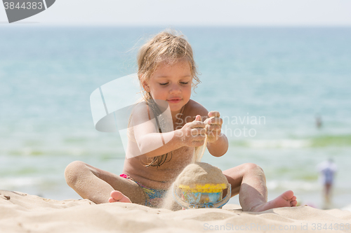 Image of Little five-year girl pours sand into bucket baby on the sea beach