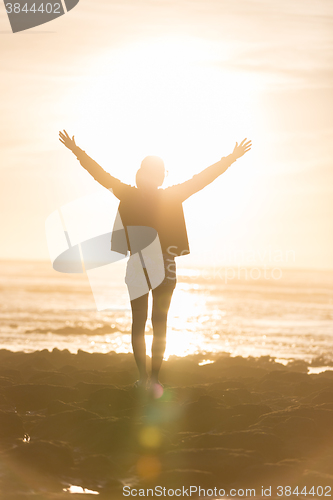 Image of Free woman enjoying freedom on beach at sunset.