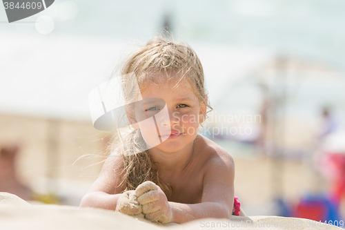 Image of Dissatisfied girl four years lies on the beach sand on his stomach and looks in the frame