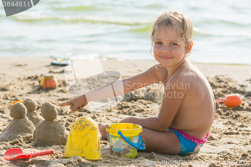 Image of Pleased with the child on a sandy beach at the water points at cakes hired by sand