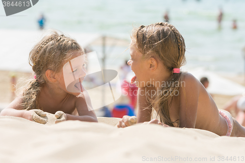 Image of Two happy little girls show each other tongues on a sandy beach