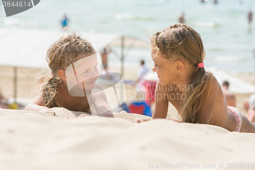 Image of Two happy little girls look at each other while lying on a sandy beach