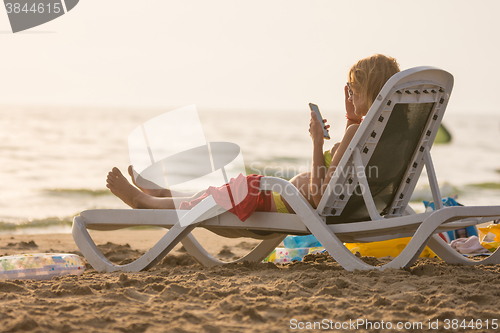 Image of Pregnant woman lying on a sun lounger on the beach and looking at the phone