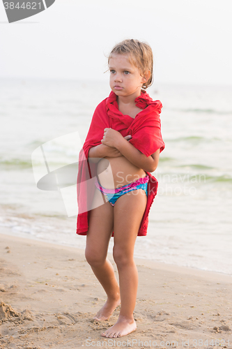 Image of Frozen five year old girl wrapped in an adult t-shirt standing on a sea shore