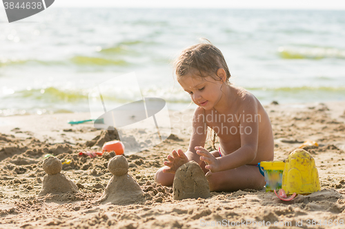 Image of The child sits on the sandy beach of the reservoir and enthusiasm molds of sand cakes