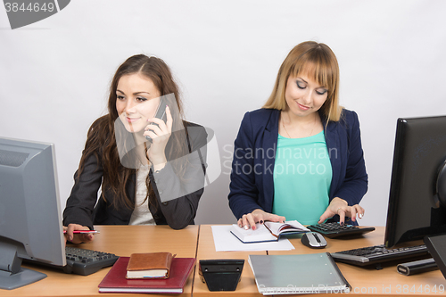 Image of  Office colleagues girl sitting behind a desk, with a phone, the other with a calculator
