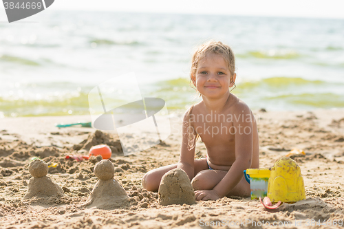 Image of The child sits on the waterfront and sculpts sand cakes