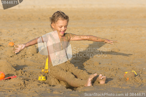 Image of Satisfied six year old girl to roll yourself wet sand on the beach