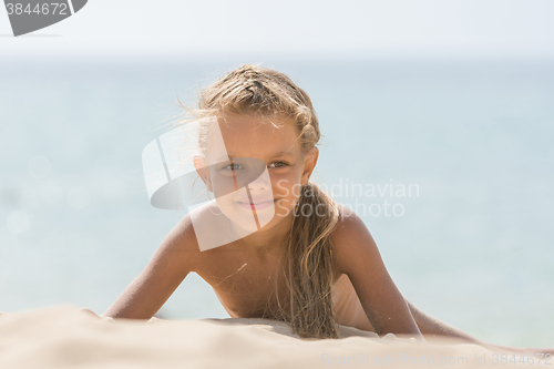 Image of Six-year Tanned girl lying on sand, leaning on hands against the sea