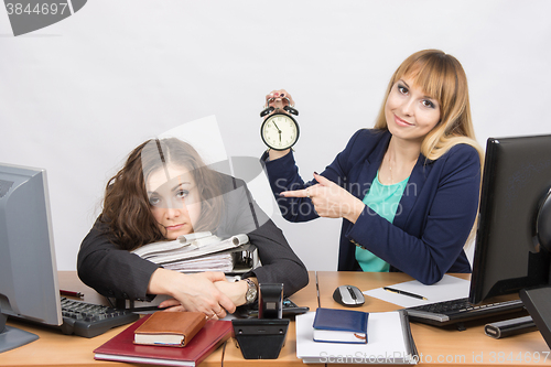 Image of The girl in the office with a smile, indicating the hours and tortured colleague