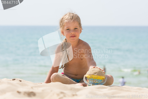 Image of Baby girl playing with sand and vederochkom child on the sea beach