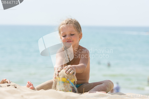 Image of Pretty girls four years playing in the sand with a child on the sea beach bucket