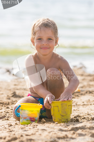 Image of Glad kid playing on a sandy beach with a pond and sand molds