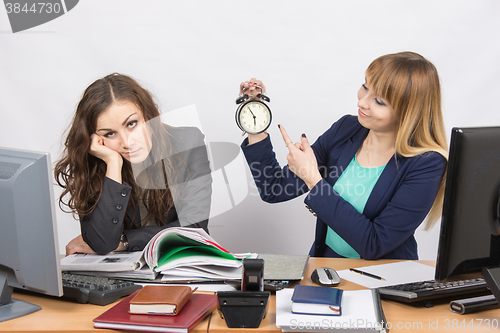 Image of  Office workers at the end of the day, one with a smile indicates a clock, another weary head props