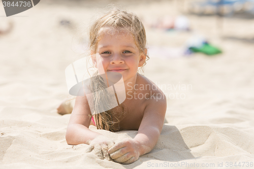 Image of Pretty girls four years lying in the sand on his stomach on the beach on a sunny day