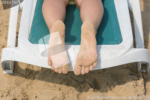 Image of On a sun lounger are female legs soiled in sand heels top