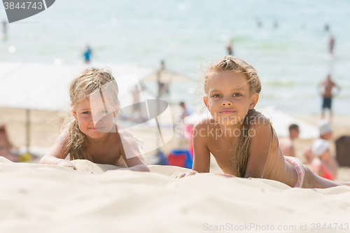 Image of Two girls lying on the sand on the beach and look at the frame