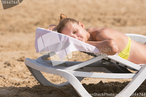 Image of Young girl is lying on a deck chair on his stomach, his head turned and eyes closed