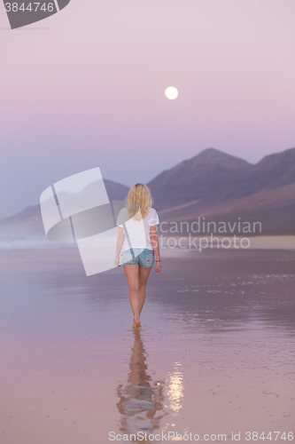 Image of Lady walking on sandy beach in sunset.