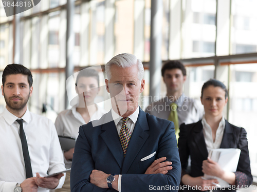 Image of portrait of senior businessman as leader  with staff in backgrou