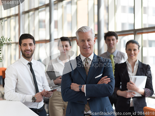 Image of portrait of senior businessman as leader  with staff in backgrou