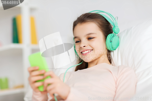 Image of happy girl lying in bed with smartphone at home