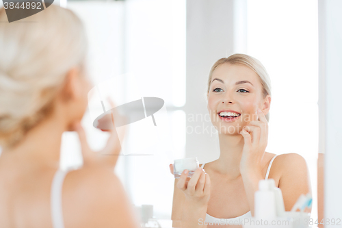 Image of happy woman applying cream to face at bathroom