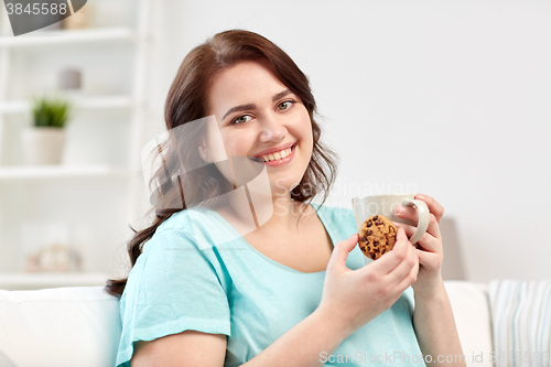 Image of happy plus size woman with cup and cookie at home