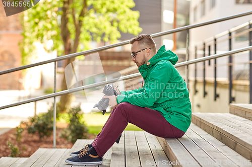 Image of young hipster man with digital camera in city