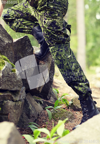 Image of close up of soldier climbing on rocks in forest