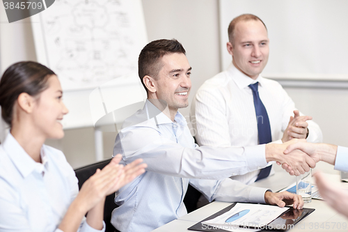 Image of smiling business team shaking hands in office