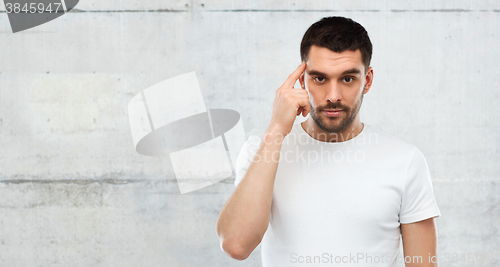 Image of man with finger at temple over gray wall