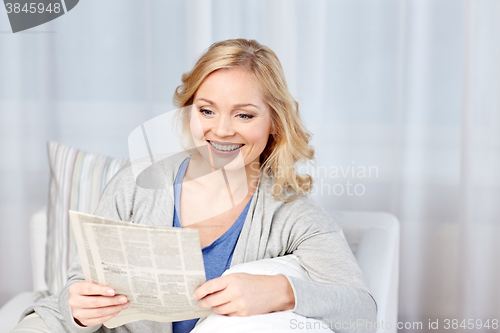 Image of smiling woman reading newspaper at home
