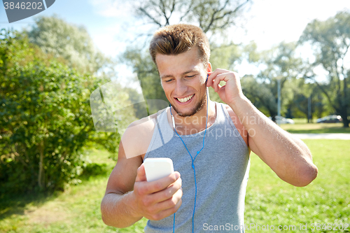 Image of happy man with earphones and smartphone at park