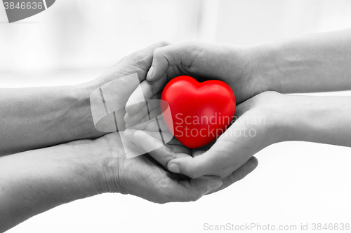 Image of senior and young woman hands holding red heart