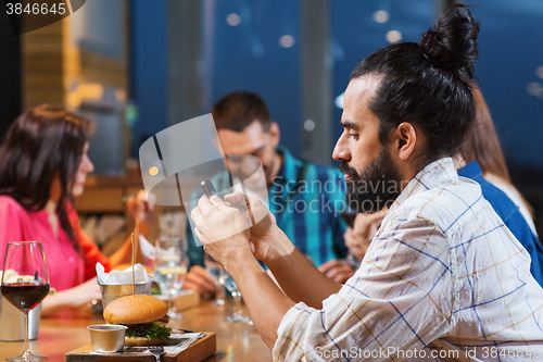 Image of man with smartphone and friends at restaurant