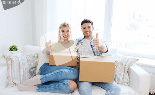 Image of happy couple with boxes showing thumbs up at home