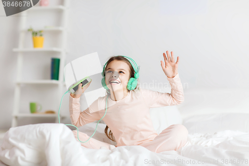 Image of girl sitting on bed with smartphone and headphones