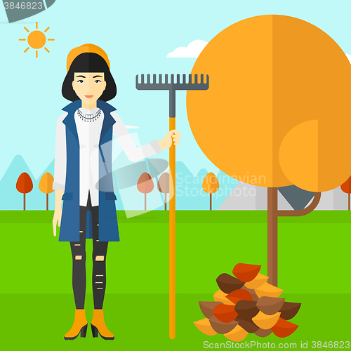 Image of Woman with rake standing near tree and heap of autumn leaves.