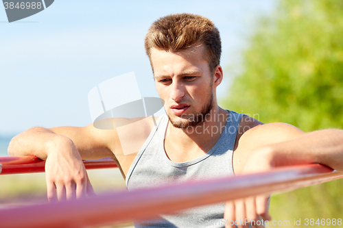 Image of young man exercising on parallel bars outdoors