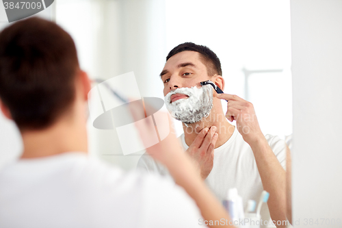 Image of man shaving beard with razor blade at bathroom