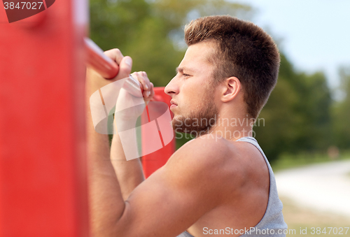 Image of young man exercising on horizontal bar outdoors